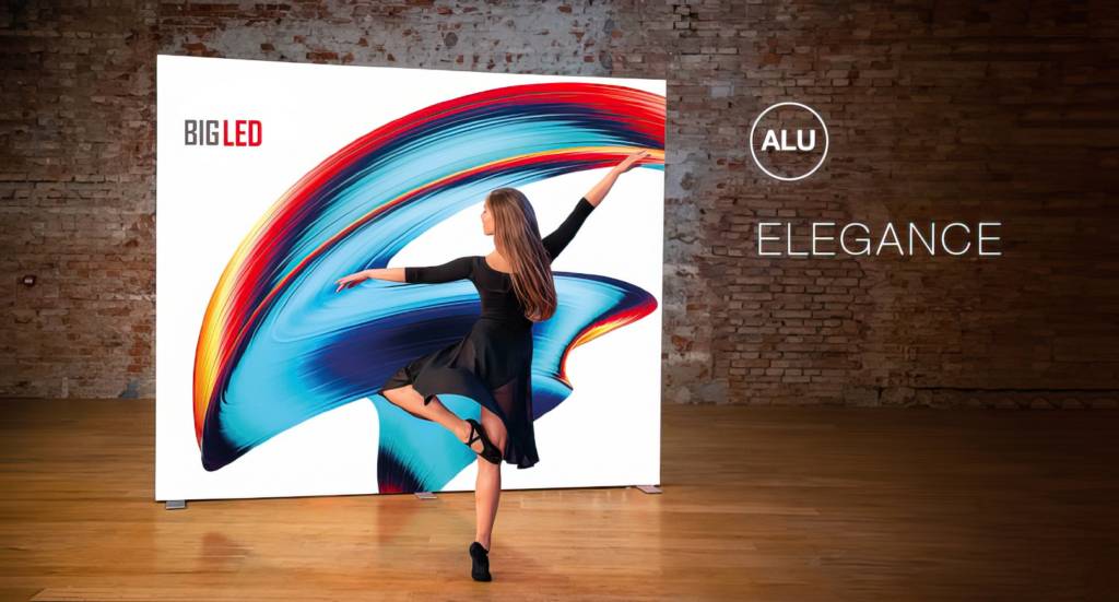 Ballerina in zwarte jurk danst voor "BIG LED" modulaire LED lightbox met levendige kleuren. "ELEGANCE" verlicht op bakstenen muur met "ALU" logo.